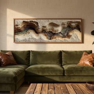 May include: A living room scene featuring a green corduroy sectional sofa with two brown leather throw pillows. A wooden coffee table with a stack of wooden trays sits in front of the sofa. A framed artwork with layered textures hangs above the sofa.