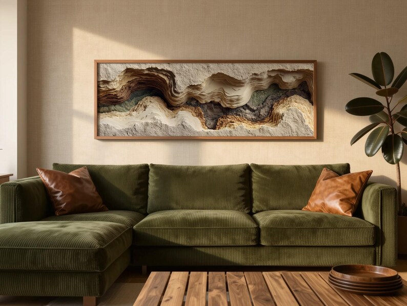 May include: A living room scene featuring a green corduroy sectional sofa with two brown leather throw pillows. A wooden coffee table with a stack of wooden trays sits in front of the sofa. A framed artwork with layered textures hangs above the sofa.