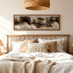 May include: A bedroom scene featuring a wooden bed frame, nightstands, and lamps with woven shades. The bed is made with white linens, beige pillows, and a textured throw. A large, framed artwork with abstract, layered textures hangs above the bed.
