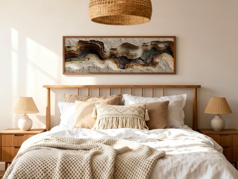 May include: A bedroom scene featuring a wooden bed frame, nightstands, and lamps with woven shades. The bed is made with white linens, beige pillows, and a textured throw. A large, framed artwork with abstract, layered textures hangs above the bed.