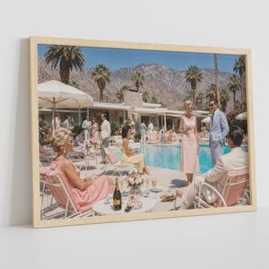 May include: A framed wall art print depicting a mid-century pool party scene with people in pastel attire lounging by a turquoise swimming pool. The background features palm trees, a modern house, and mountains under a clear blue sky.
