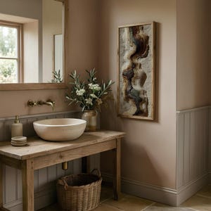 May include: A rustic bathroom scene featuring a wooden vanity with a stone vessel sink. A framed abstract artwork hangs on the wall. A mirror and a wicker basket add to the room's natural aesthetic. A vase of flowers sits on the vanity.