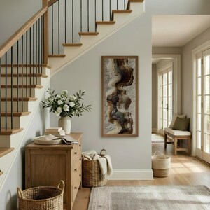 May include: A well-lit entryway with a wooden staircase, a framed abstract art piece, and a wooden chest of drawers. A white vase with flowers sits on the chest. Wicker baskets and a rug add to the decor.