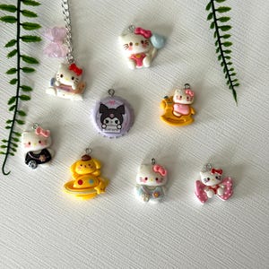 May include: A collection of colorful Hello Kitty and Sanrio character charms. The charms include Hello Kitty in various outfits, a dog character, and a purple charm with a black character. Each charm has a silver loop for attaching to a keychain or necklace.