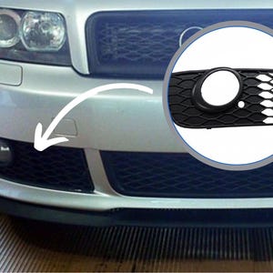 May include: Close-up of a silver car's front bumper with a black mesh grille. A circular inset highlights a black fog light cover with a honeycomb pattern and a round opening. Automotive parts.
