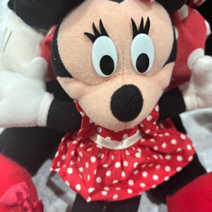 May include: A Minnie Mouse plush doll with a red and white polka dot dress and bow. The doll has black ears, a black nose, and large, light blue eyes. The doll's arms and legs are black, and it has red shoes.