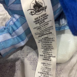 May include: A white tag with the Disney logo and text in multiple languages, including English, French, and Spanish. The tag indicates the product was made in Vietnam and includes the shopDisney.com website address.