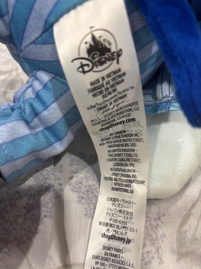 May include: A white tag with the Disney logo and text in multiple languages, including English, French, and Spanish. The tag indicates the product was made in Vietnam and includes the shopDisney.com website address.
