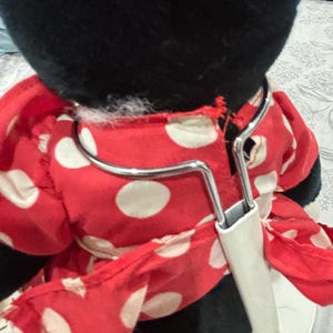 May include: A plush toy featuring a black head and a red dress with white polka dots. The dress is held by a metal hanger with a white plastic piece. The toy is a classic character.