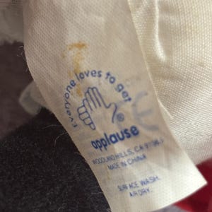 May include: A white fabric tag with the word "applause" in blue, along with the text "Everyone loves to get" and a hand graphic. The tag also includes washing instructions.