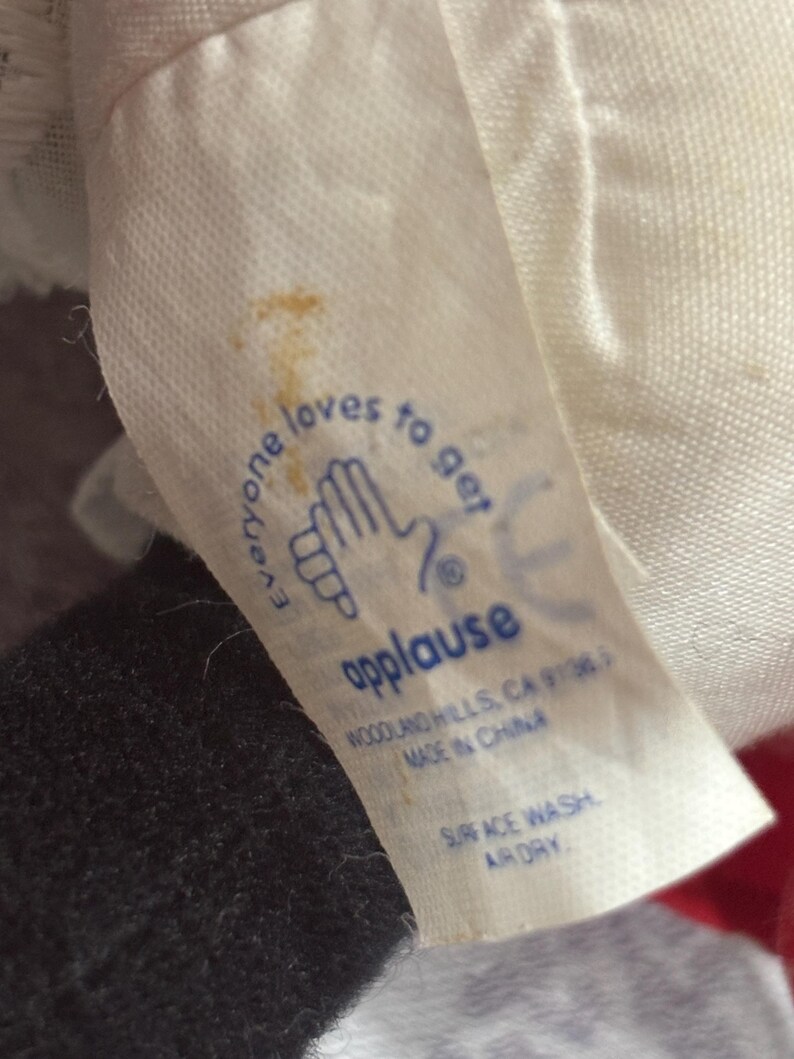 May include: A white fabric tag with the word "applause" in blue, along with the text "Everyone loves to get" and a hand graphic. The tag also includes washing instructions.