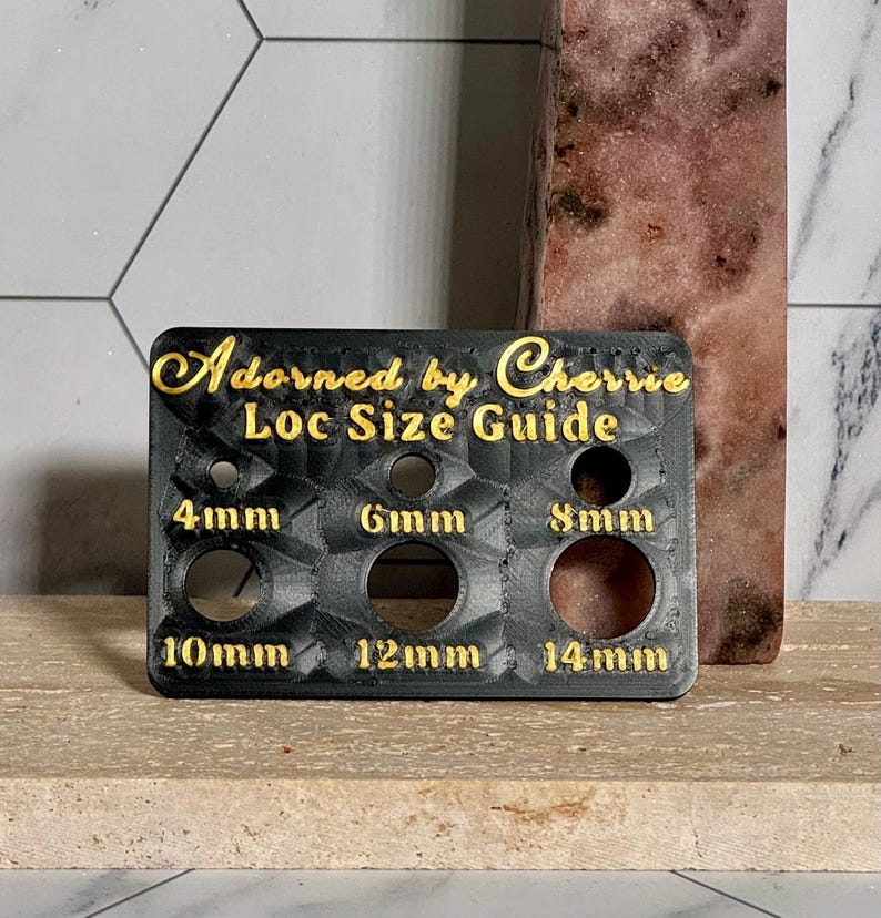 Puede incluir: Una gu&iacute;a de tama&ntilde;o de loc negro con letras doradas que dice "Adorned by Cherrie". La gu&iacute;a tiene agujeros etiquetados 4 mm, 6 mm, 8 mm, 10 mm, 12 mm y 14 mm. La gu&iacute;a est&aacute; sobre una superficie marr&oacute;n claro.