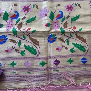 May include: A beige textile with a floral and peacock design. The design features peacocks, flowers, and leaves in shades of blue, red, green, and purple. The bottom edge has a pink border with tassels.