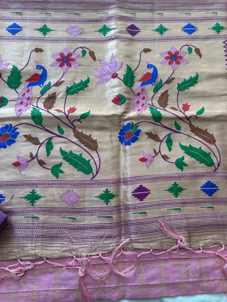 May include: A beige textile with a floral and peacock design. The design features peacocks, flowers, and leaves in shades of blue, red, green, and purple. The bottom edge has a pink border with tassels.