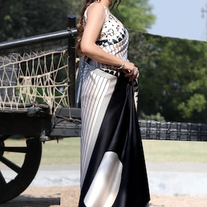Puede incluir: Vestido sin mangas con estampado en blanco y negro con falda negra fluida. El vestido presenta un dise&ntilde;o geom&eacute;trico en el corpi&ntilde;o y rayas verticales en la falda. Un gran dise&ntilde;o ovalado blanco est&aacute; en la falda.