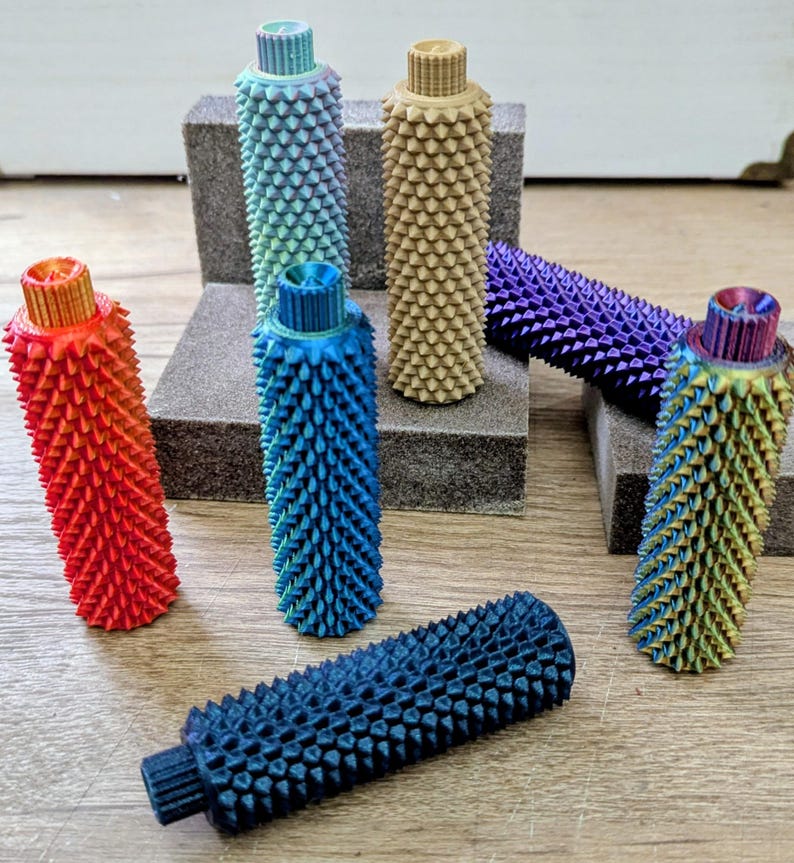Puede incluir: Una colecci&oacute;n de objetos cil&iacute;ndricos texturizados y coloridos con una superficie puntiaguda. Los objetos son de varios colores, incluyendo rojo, azul, verde y morado. Los objetos est&aacute;n dispuestos sobre una superficie de madera y bloques grises.