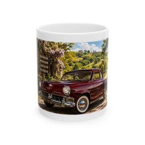 May include: A white ceramic mug featuring a printed image of a dark red vintage Studebaker car parked on a dirt road. The scene includes a wooden signpost with text reading Scenic Drive, Vineyard 5 mi, Lake 3 mi, and Picnic Area, set against green hills.