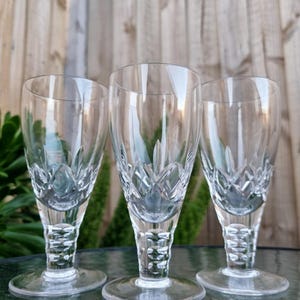 May include: Three clear glass goblets featuring a cut diamond pattern on the lower bowl and a textured, faceted stem design. Each glass has a smooth, circular base and a tapered rim, showcasing a reflective, transparent finish throughout.