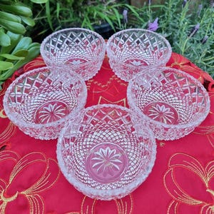 May include: A set of five clear glass bowls featuring a pressed diamond pattern on the exterior sides and a starburst design etched into the centre of the base. Each bowl has a circular rim and a thick, transparent construction with reflective facets.