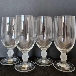 May include: Four clear crystal Mikasa wine glasses. Each glass has a rounded bowl, a frosted stem with a bulbous design, and a clear, circular base. The glasses are labelled "Crystal Mikasa W. Germany".