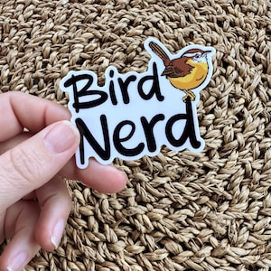 May include: A white sticker with black text that reads "Bird Nerd" and a cartoon image of a brown and yellow bird.