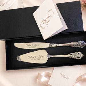 May include: A silver-toned cake knife and server set with ornate handles, engraved with the names Audrey & Kenny and the date 02.16.2025. The set is presented in a black rectangular gift box alongside a white card with the text Thank You.