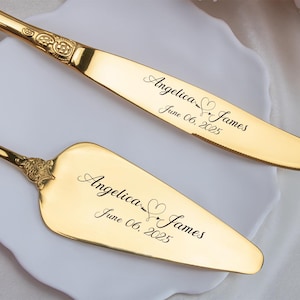 May include: A gold-colored cake knife and server set. The knife and server have ornate handles and are engraved with the names "Angelica & James" and the date "June 06, 2025". The set is displayed on a white plate.