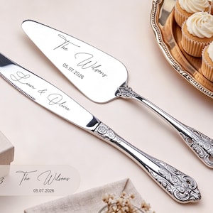 May include: A silver cake knife and server set with ornate embossed handles. The knife is engraved with the text Liam & Olivia, and the server is engraved with The Wilsons and the date 05.07.2026 in a black script font on the polished metal.