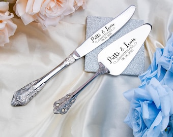 May include: Silver cake knife and server set with ornate handles. The knife has a serrated edge. Both pieces are engraved with "Patti & Lewis" and the date "08.16.2025". The set is displayed with floral decorations.