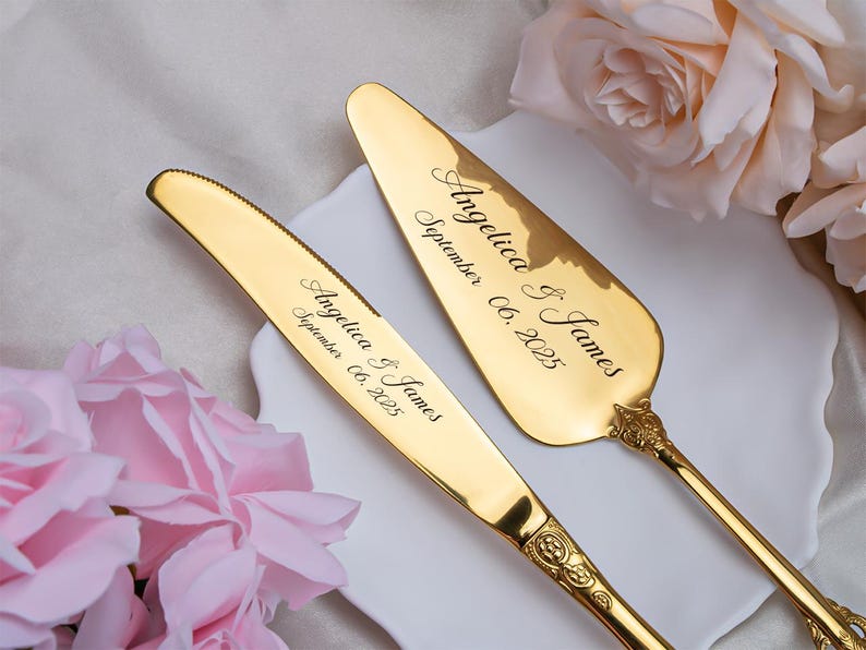 May include: A gold-colored cake knife and server set. The knife and server are engraved with the names "Angelica & James" and the date "September 06, 2025". The set is displayed on a white plate with pink roses in the background.