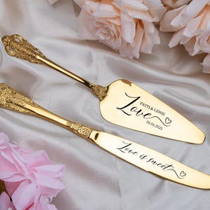 May include: Gold-colored cake server and knife set with ornate handles. The server has the word "Love" and the names "Patti & Lewis" with a date. The knife has the phrase "Love is sweet". Perfect for weddings.