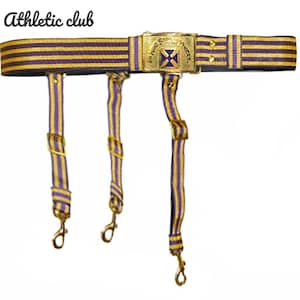 May include: A purple and gold striped belt with three suspender straps. The belt features a gold buckle with a blue cross design and the text "In Hoc Signo Vinces". The words "Athletic club" are in the upper left corner.