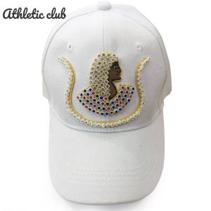 Könnte beinhalten: Weiße Baseballkappe mit einem dekorativen Design, das das Profil einer Person mit einem Perlenkopfschmuck und farbenfrohen Akzenten zeigt. Der Text "Athletic club" befindet sich oben links auf der Kappe.