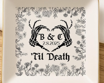 May include: A square, off-white ceramic trinket dish with a gold rim. The center features a black floral design and a heart formed by skeleton hands, with the text "B & C 2.8.2025" and "'Til Death".