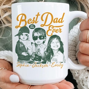 May include: A white ceramic mug featuring the mustard yellow text Best Dad Ever and EST. 2020 above a black and white photograph of three children wearing sunglasses. The names Sophia, Jackson, and Emily are printed in yellow below the children.