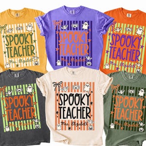 May include: Six short-sleeve t-shirts in yellow, purple, orange, dark gray, cream, and olive green. Each shirt features a graphic with vertical stripes, the text "SPOOKY TEACHER" and "Mrs. Elizabeth," plus small illustrations of ghosts, bats, and spiders.