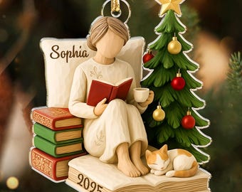 May include: A Christmas ornament featuring a person reading a book, with a cat, a Christmas tree, and a stack of books. The ornament has the name "Sophia" and the year "2025" on it. The tree is decorated with red and gold ornaments and a gold star.