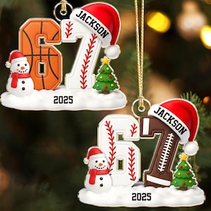 May include: Christmas ornaments featuring the number 67 with sports themes. One ornament has a basketball design, the other a baseball and football design. Each has a Santa hat with the name "JACKSON" and the year "2025".
