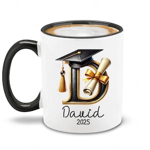 May include: White ceramic coffee mug with a black handle and rim. The mug features a black and gold graduation cap and diploma with the letter "D" in the center. The name "Dawid" and the year "2025" are printed below the design.