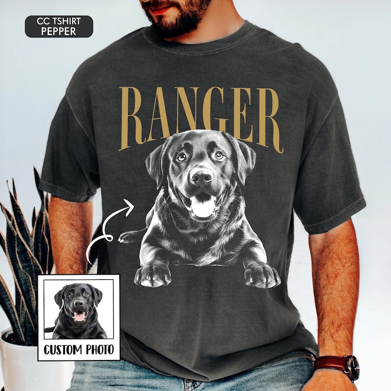 May include: Dark gray t-shirt featuring a black and white illustration of a Labrador Retriever with the word "RANGER" in gold lettering. A small image of the dog is in the lower left corner with the text "CUSTOM PHOTO".