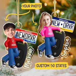 May include: Customizable Christmas ornaments featuring cartoon figures with license plates that read "NEW DRVR" and car keys. One ornament has "Matthew" and the other has "Sophia" written on it. The text "YOUR PHOTO" and "CUSTOM 50 STATES" are also visible.