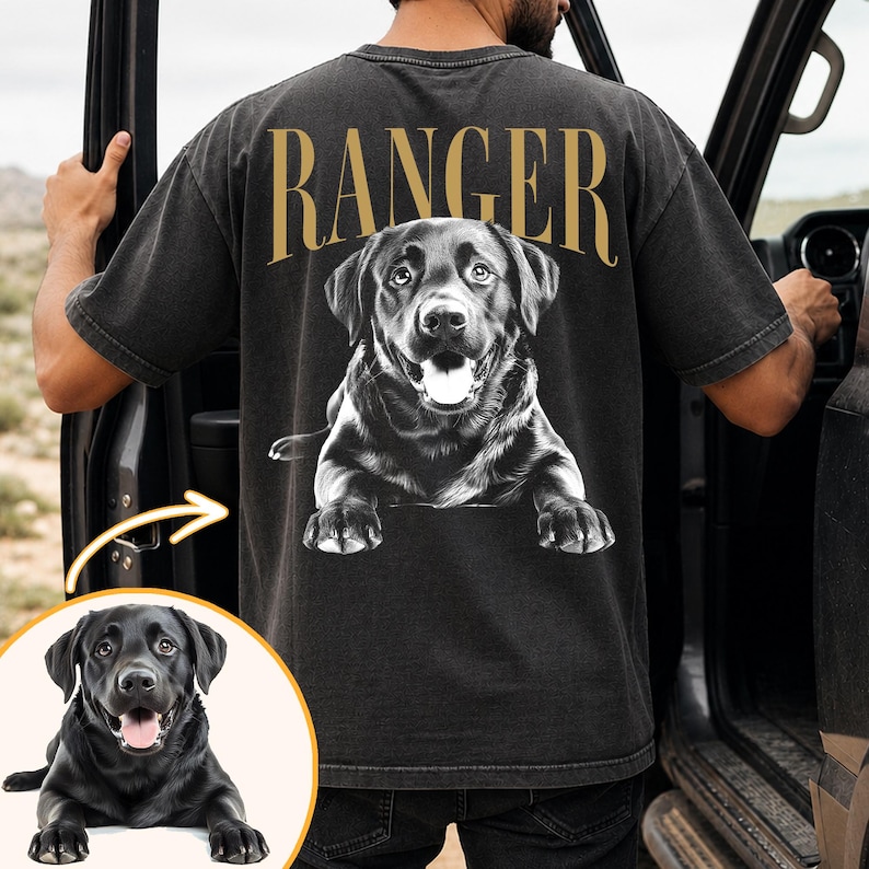 May include: Dark grey t-shirt featuring a black and white Labrador Retriever graphic and the word "RANGER" in gold. The dog is shown with its tongue out. The shirt is worn by a person.