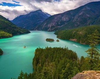 May include: A panoramic view of a lake surrounded by lush green mountains. The water is a vibrant turquoise color and there are several small islands in the lake. The sky is partly cloudy.
