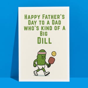Peut inclure: Une carte de vœux pour la fête des pères avec le texte "HAPPY FATHER'S DAY TO A DAD WHO'S KIND OF A BIG DILL." La carte représente un cornichon de dessin animé jouant au pickleball. Le cornichon est vert.