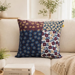 May include: A square throw pillow featuring a patchwork design composed of four distinct floral patterns. The sections display motifs of small yellow flowers on maroon, blue flowers on navy, light flowers on blue, and maroon flowers on white.