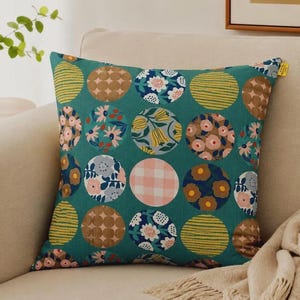 May include: A square throw pillow with a teal green background featuring a repeating pattern of circles. Each circle contains different designs, including floral prints, yellow and green stripes, brown geometric shapes, and a pink and white gingham check.