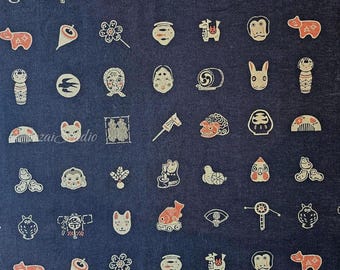May include: A navy blue fabric with a repeating pattern of Japanese-style illustrations in white and red. The illustrations include animal faces, flowers, and other cultural symbols. The fabric has a slightly textured appearance.