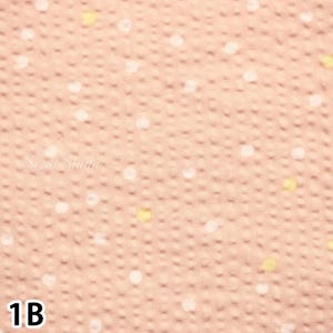May include: Close-up of a peach-colored fabric with a dotted pattern. The dots are white and yellow, scattered across the textured surface. The text "Sezai Studio" is visible in the center, and the number "1B" is in the bottom left corner.
