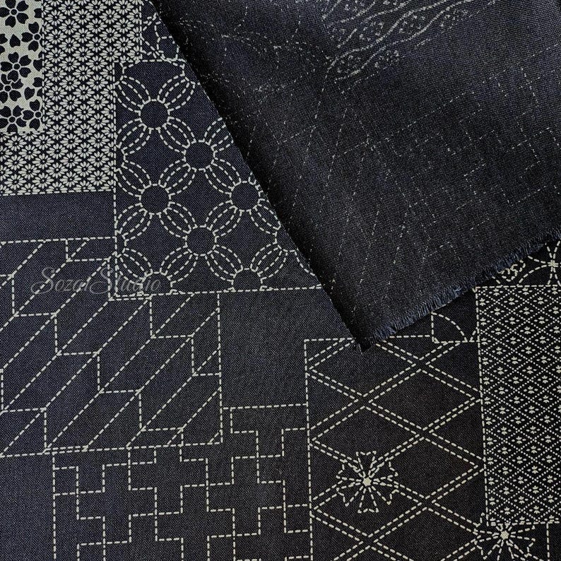 May include: A dark navy blue fabric featuring a patchwork design of white geometric patterns and floral motifs reminiscent of sashiko stitching. The textile displays various squares with intricate lines, crosses, and circles, with the text Sozai Studio.