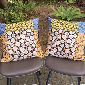 Peut inclure: Deux coussins carr&eacute;s pr&eacute;sentant un motif patchwork de tissus &agrave; fleurs. Les motifs incluent des fleurs jaunes sur fond sombre, des imprim&eacute;s floraux violet clair et un panneau central de fleurs blanches et roses sur fond brun fonc&eacute;.